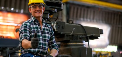 Front view of smart technician or engineer worker with protective helmet stand with confident and thumbs up in factory workplace. Concept of good system of management get better industrial business.